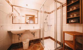 A modern bathroom with a shower and two sinks. There is a wooden shelf and a bright, friendly atmosphere.