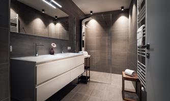 A modern bathroom with elegant gray tiles and a spacious shower. The room is well-lit and has a minimalist wash area.