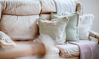 A comfortable sofa with several decorative cushions in soft colors. A cozy atmosphere is conveyed through the soft textiles and the relaxed arrangement.