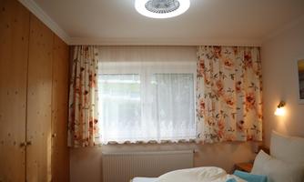 A cozy bedroom with wooden furniture and floral curtains. The light falls through the window, creating an inviting atmosphere.