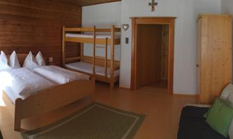 A cozy room with a double bed and a bunk bed. The walls are made of wood, and there is a sofa as well as a television.