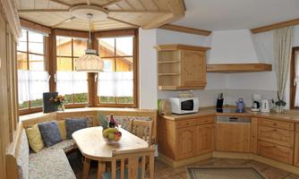 A bright kitchen with wooden cabinets and a cozy dining area. Large windows provide plenty of daylight and a pleasant atmosphere.