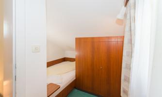 A simple bedroom with a wooden wardrobe and a single bed. The room has a bright, friendly impression.