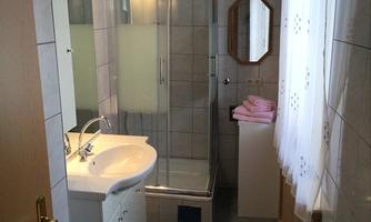 A small bathroom with a shower stall and a sink. The room has bright tiles and window decor with curtains.