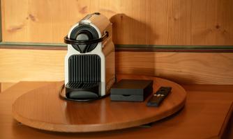 A Nespresso machine is placed on a round wooden tray. Next to it lies a small black box and a remote control.
