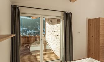 A modern bedroom with a large window and access to a balcony. The room has bright walls and wooden details.