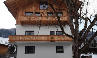A modern chalet with timber cladding and a balcony. It stands in the snow in front of a winter landscape.