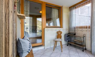 A bright room with large windows and a cozy chair. The interior is modern and inviting, with a mix of wooden and textile elements.