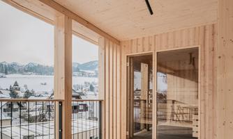 A modern wooden balcony with clean lines and plenty of natural light. In the background, snow-covered mountains and a peaceful view of the surroundings can be seen.