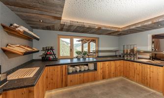 A modern kitchen with wooden shelves and an elegant countertop. Generous windows provide a beautiful view of the landscape.