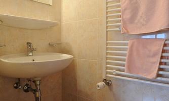 A small bathroom with tiled walls and a sink. Towels in soft colors hang on a radiator.