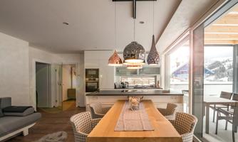A modern kitchen with a large dining table and stylish chairs. Large windows offer a view of the winter landscape.
