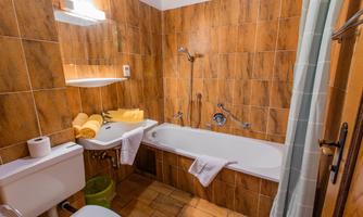 A simple bathroom with brown tiles and a bathtub. It also includes toilet paper, towels, and basic sanitary facilities.