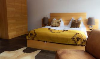 A cozy bedroom with a large bed, yellow blankets, and two nightstands. The decor is modern with wooden accents and a stylish armchair.