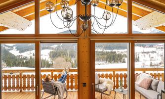 A cozy atmosphere in a wooden house with a view of snow-covered mountains. A person relaxes on the terrace and enjoys the view.