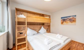 A cozy bedroom with a bunk bed and a double bed. The wooden furniture and the bright design create an inviting atmosphere.