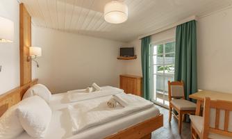 A cozy hotel room with two beds and a bright color scheme. A table and chairs complement the decor, and the window offers daylight.