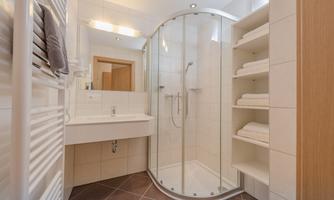 A modern bathroom with a glass shower cabin. It is bright and offers towels and a sink area.