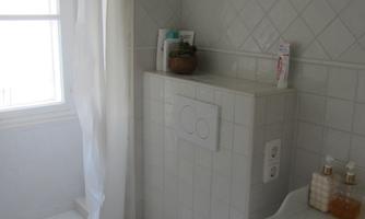 A small bathroom with a shower, toilet, and sink. The walls are tiled in light colors and there is a window that lets in daylight.