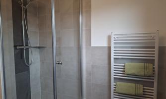 A modern bathroom with a glass shower and a towel warmer. The towels are in a fresh green color.