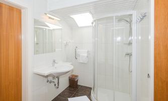 A modern bathroom with a shower, a sink, and a large wall mirror. The walls are tiled white and the floor is dark.