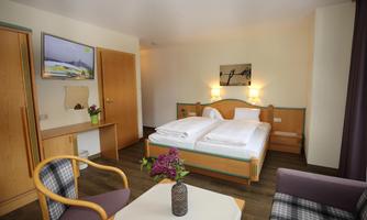 A cozy room with two single beds, woodwork, and modern furniture. A small table with a vase and fresh flowers complements the decor.