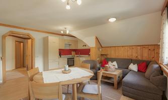 A cozy living area with a bright, modern kitchen and a dining area. The seating area is furnished with a gray sofa and decorative cushions.