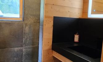 A modern bathroom with wooden details and black tiles. There is a window that lets in natural light.
