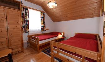 A cozy room with two single beds and wooden paneling. There is a wardrobe and a window with colorful curtains.