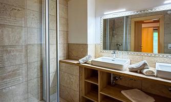 A modern bathroom with a shower and a wooden ceiling. There is a sink and towels on the shelf.
