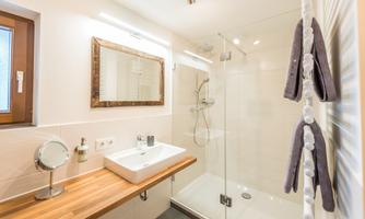 A modern bathroom with a shower and a wooden vanity. The space is brightly lit and has a clear, clean aesthetic.