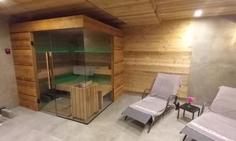 A modern wellness area with a wooden sauna and comfortable loungers. The room has a cozy atmosphere with warm light.