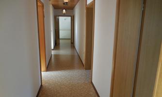 A bright hallway with wooden ceilings and several doors. The floor is adorned with a carpet pattern.