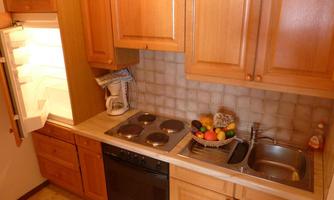 A cozy kitchen with wooden furniture and an open refrigerator door. On the countertop, there is a kettle and a bowl of fresh fruit.