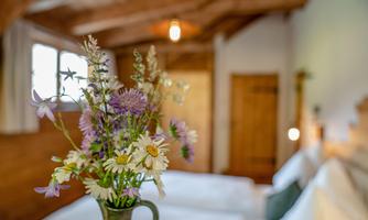 A cozy bedroom with two beds and a beautiful vase filled with fresh flowers. Bright wood decor and warm light accents create an inviting atmosphere.