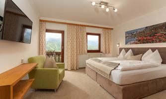 A modern bedroom with a large bed and a cozy armchair. The windows offer a direct view of the Dachstein, the surrounding mountains, and the beautiful nature.
