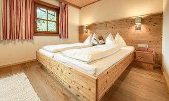 A cozy bedroom with a wooden bed and a warm atmosphere. Large windows let in plenty of light and offer a view outside.
