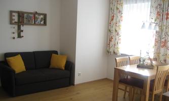 A modern living room with a gray sofa and two yellow cushions. A wooden coffee table is next to a window with colorful curtains.