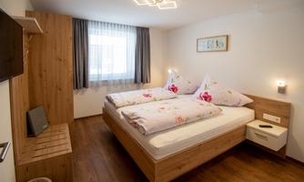 A cozy bedroom with a large bed and wooden decor. It has a window with curtains and modern lighting.