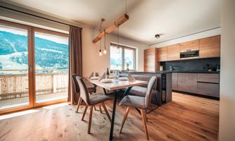 A modern dining room with a wooden chair and a table. Large windows offer a view of the mountains.