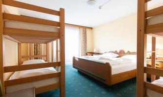 A bright room with two bunk beds and a double bed. The room has large windows that let in plenty of daylight.