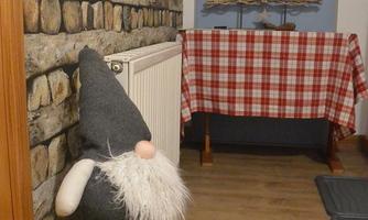 A cozy room with a stone wall and a decorative little gnome. In the background, there is a table with a checkered tablecloth and candles.