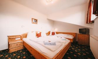 A cozy room with two single beds and wooden furniture. The walls are bright and the carpet has a colorful pattern.