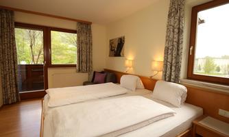 A bright bedroom with a double bed and two windows. The room is decorated in a modern style and has a view of the outdoors.
