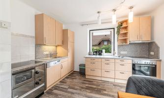 A modern kitchen with wooden cabinets and a bright color scheme. It features large windows that let in plenty of light.