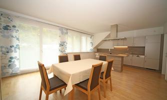 A modern dining room with a rectangular table and chairs. The room has large windows and a bright, inviting atmosphere.