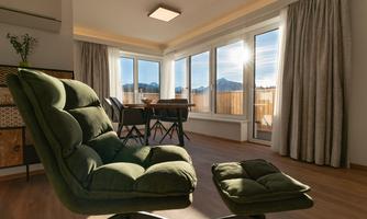 A cozy room with large windows and a view of the mountains. Furnished with a green armchair and a table with chairs.