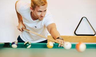 A young man is playing pool billiards. He is focusing on his next shot.