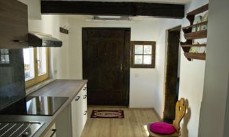 A bright kitchen with modern appliances and a rustic wooden stove. A striking pink chair stands in the room.