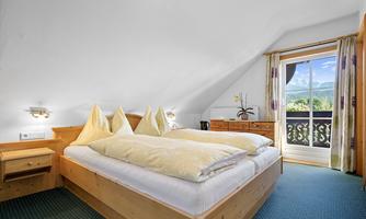 A cozy bedroom with a double bed and two pillows. The room has large windows with a view of the mountains and a balcony.